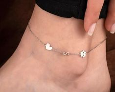 a woman's foot wearing a silver ankle bracelet with hearts and clovers on it