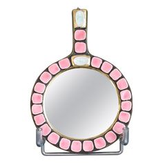 a round mirror with pink and white designs on the front, hanging from a metal stand