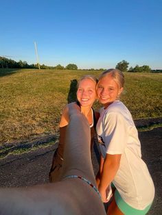 two women are standing next to each other in front of an open field with a horse