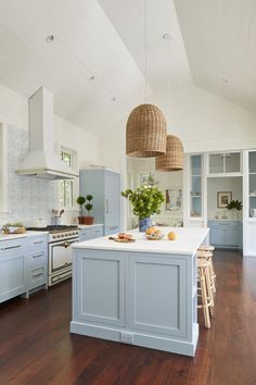 a kitchen with blue cabinets and white counter tops, wooden flooring and hanging lights above the island