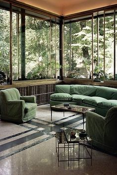 a living room filled with lots of green furniture next to large windows and floor to ceiling windows