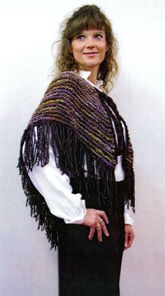 a woman wearing a purple and black shawl standing in front of a white wall