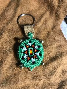 a beaded keychain with a green turtle on it's side sitting on a bed