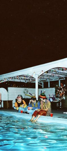 people sitting on the edge of a swimming pool at night