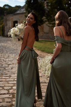 two beautiful women standing next to each other on a cobblestone road in front of an old building