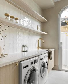 a washer and dryer in a room with white tile walls, open shelving