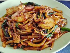 a white plate topped with stir fried noodles and meat on top of vegetables next to corn