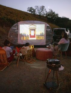 people sitting in chairs watching a movie on an outdoor projector screen at night time