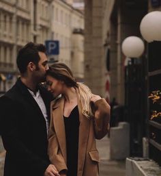 a man and woman standing next to each other in front of a building on a city street