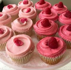 there are many cupcakes with pink frosting and raspberries on top