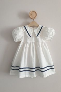 Introducing our charming White Cotton Sailor Dress for baby girls! This delightful dress is designed to make your little princess look absolutely adorable during sunny summer days. Crafted from high-quality cotton, this dress offers a lightweight and breathable feel, ensuring maximum comfort for your baby girl. The soft fabric is gentle on her delicate skin, making it ideal for all-day wear. The dress features a classic sailor-inspired design that adds a touch of timeless elegance to your baby's Preppy White Ruffled Dress, Cute Doll Collar Summer Dresses, Cute Summer Dresses With Doll Collar, Cute Doll Collar Dresses For Summer, White Sweet Style Puff Sleeve Dress, White Summer Dress For School, Cotton Puff Sleeve Playtime Dresses, Summer Baptism Dress With Puff Sleeves, Summer Puff Sleeve Baptism Dress