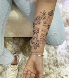 a woman's arm with a cross and flowers tattoo on her left hand, while sitting on the floor