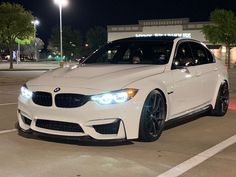 a white car is parked in a parking lot at night time with its lights on