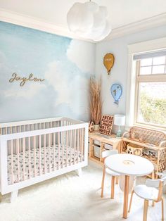 a baby's room decorated in blue and white with clouds painted on the wall