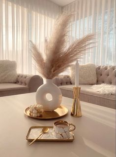 a white table topped with a vase filled with feathers next to a candle and tray