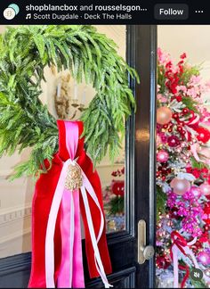 a christmas wreath is hanging on the front door with pink and red decorations behind it