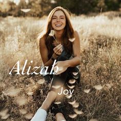 a woman sitting on the ground holding a flower in her hand and smiling at the camera