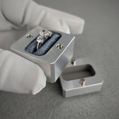 a pair of engagement rings sitting in a silver ring box on top of a white glove