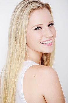 a woman with long blonde hair smiling at the camera while wearing a white tank top