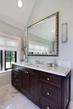 a large bathroom with marble counter tops and wooden cabinetry, along with a mirror on the wall