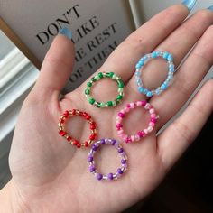 three different colored beaded bracelets are held in someone's hand with a book behind them