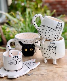 three coffee mugs with cats painted on them sitting on a table next to each other