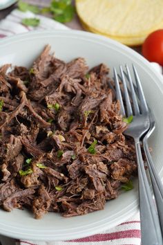 a white plate topped with shredded meat and vegetables next to a fork on top of a table