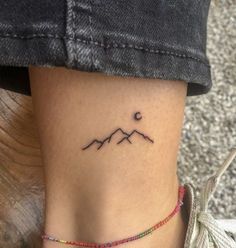 a small tattoo on the side of a woman's leg, with mountains in the background