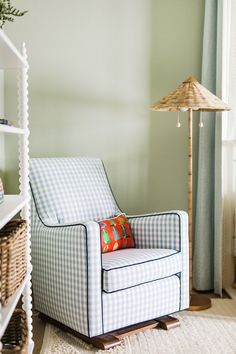 a blue and white chair sitting in front of a window next to a shelf filled with baskets