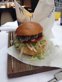 a hamburger sitting on top of a wooden cutting board next to a knife and fork