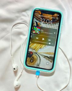 an iphone with ear buds hooked up to it on a white sheet covered bed next to headphones