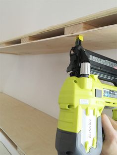 a person holding a drill in their right hand and drilling the bottom part of a shelf