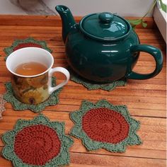 a tea pot sitting on top of a wooden table next to two crocheted coasters