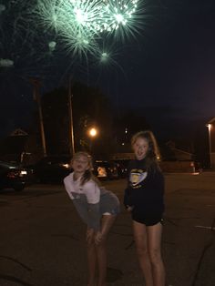 two girls are standing in the parking lot with fireworks