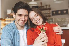 a young man and woman are smiling at the camera while holding a bouquet of flowers