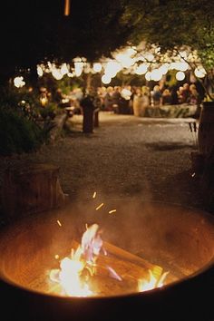 an open fire pit in the middle of a park at night with people sitting around it