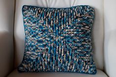 a blue and white knitted pillow sitting on top of a chair