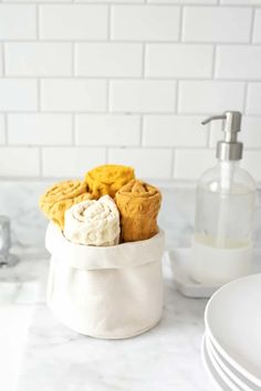 some cookies are in a white bowl on the counter next to plates and soap dispenser