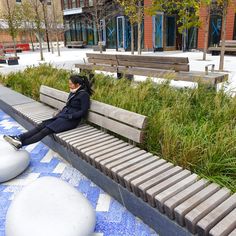 a woman sitting on top of a wooden bench next to tall grass covered park benches