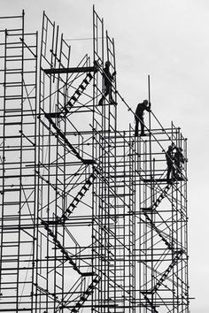 two men working on scaffolding at the top of a tall building in black and white