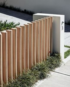 a wooden fence is lined with plants and grass in front of a white box on the sidewalk