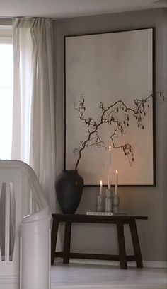 a table with two candles on it next to a vase and painting in the background