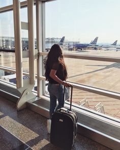 a woman standing next to an airport window with her luggage