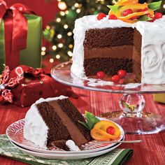 two slices of chocolate cake with white frosting and fruit toppings on plates next to a christmas tree