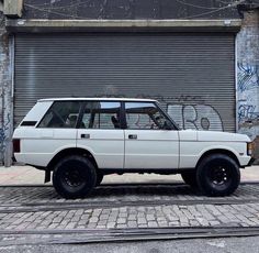 an old white station wagon parked in front of a garage door with graffiti on it