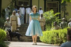 a woman in a blue dress is walking down the street with other people behind her