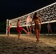 people are playing volleyball on the beach at night with lights strung across the sand and in front of them