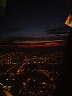 the view from an airplane window at night with city lights in the distance and dark clouds