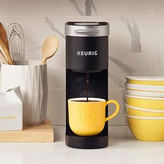 a keurig coffee maker with yellow cups and wooden spoons next to it