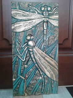 a metal plaque with a dragonfly on it's back and two other dragonflies in the background